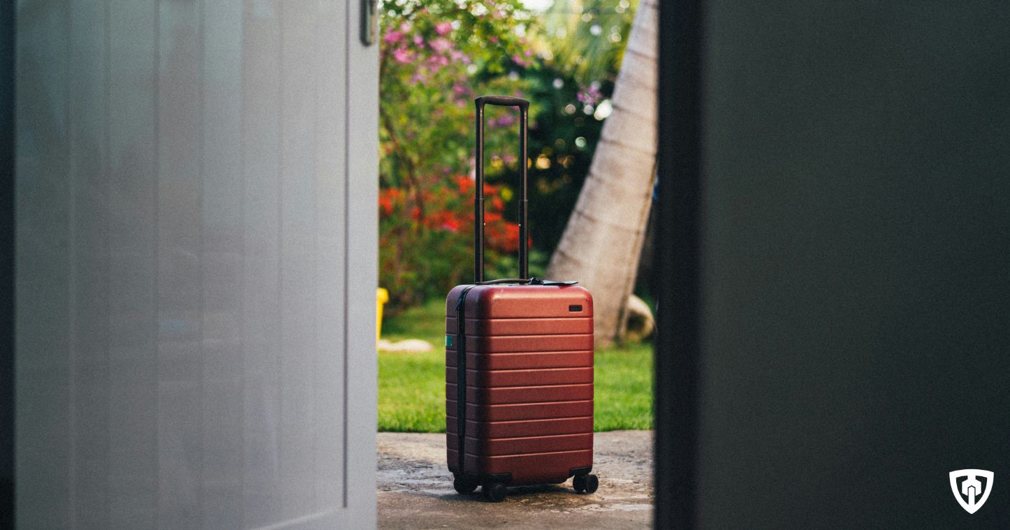 Imagen de una maleta de viaje frente a una puerta abierta, transmitiendo la importancia de proteger tu hogar cuando te vas de vacaciones. Una cerradura de alta seguridad es lo mejor para irte tranquilo y volver con la misma paz.